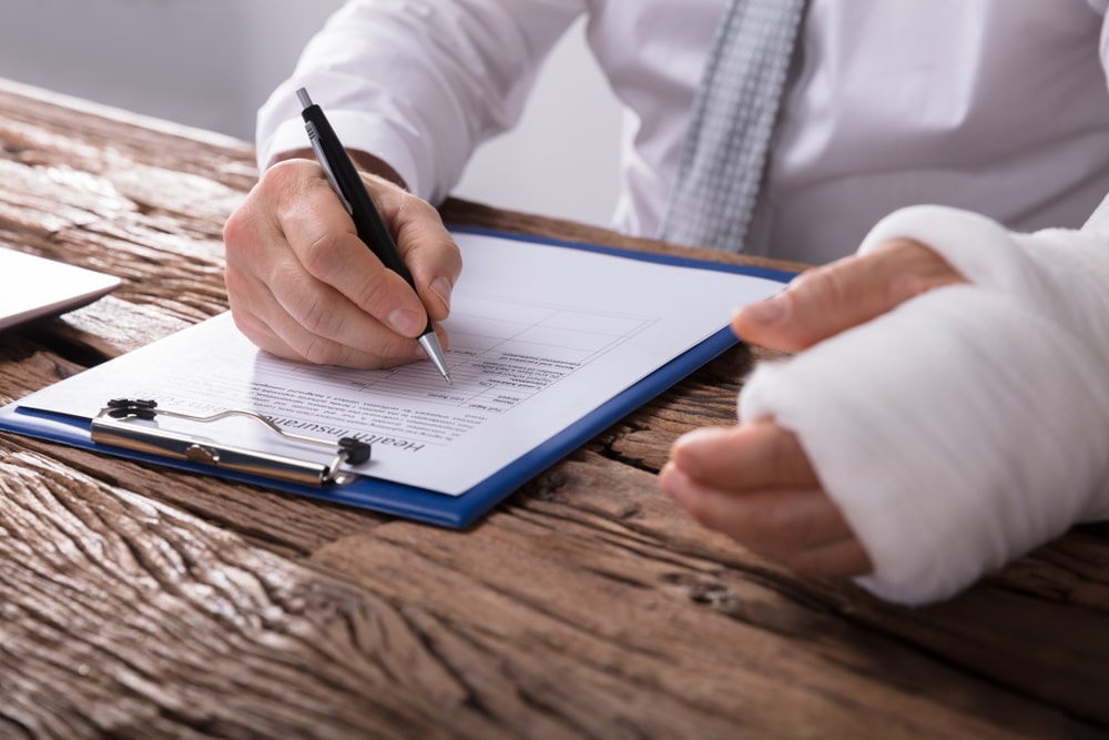 Close-up of a businessperson with broken arm filling out health insurance