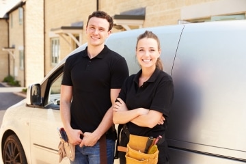 Two tradies smiling and standing against a van