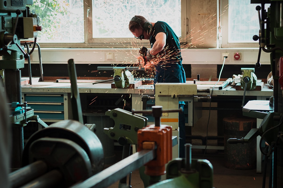 Man in workshop surrounded by equipment, using an angle grinder with orange sparks flying from the tool