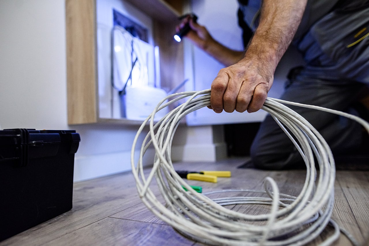 Electrician holding wires and flashlight, working on modem