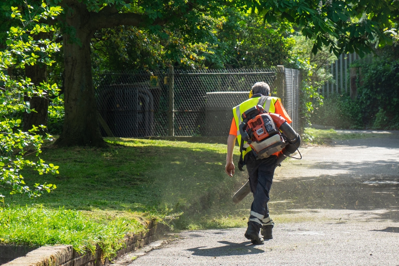 A landscape gardener using a leaf blower to blow away freshly cut grass